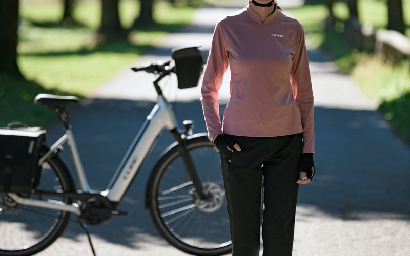Radfahrerin steht neben ihrem CUBE Trekking-E-Bike auf einem Weg im Park