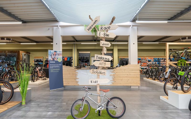 Holzwegweiser zu Race, E-Bike, Werkstatt, Trekking, MTB, Bekleidung und Kids im Verkaufsraum