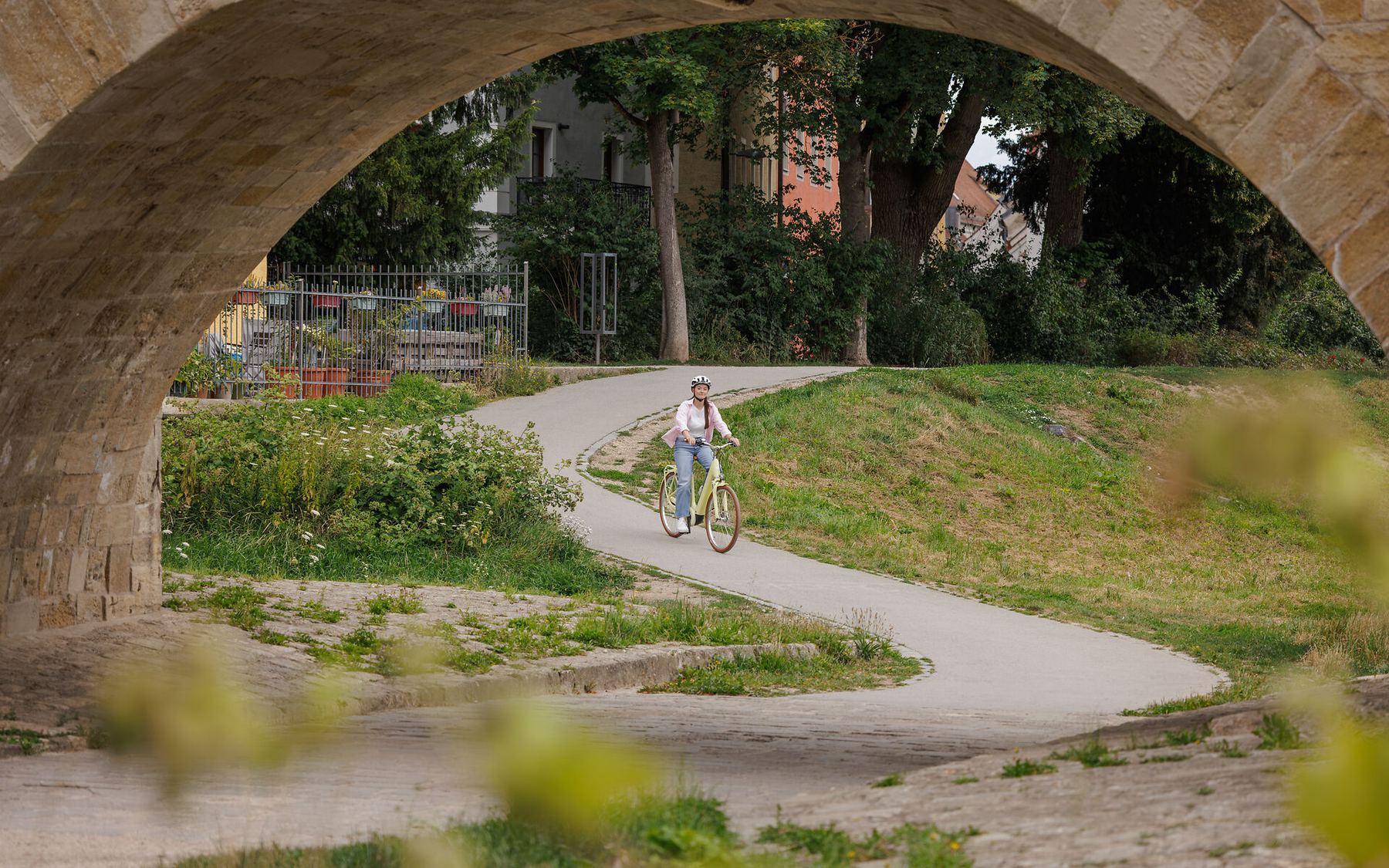 Radfahrerin auf einem City-Rad auf einem Uferweg unter einem Steinbrückenbogen