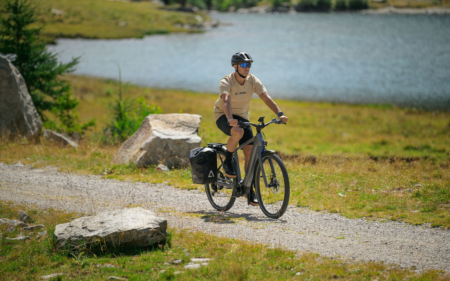 Radfahrer auf einem CUBE Trekkingrad mit Packtasche auf einem Schotterweg am See