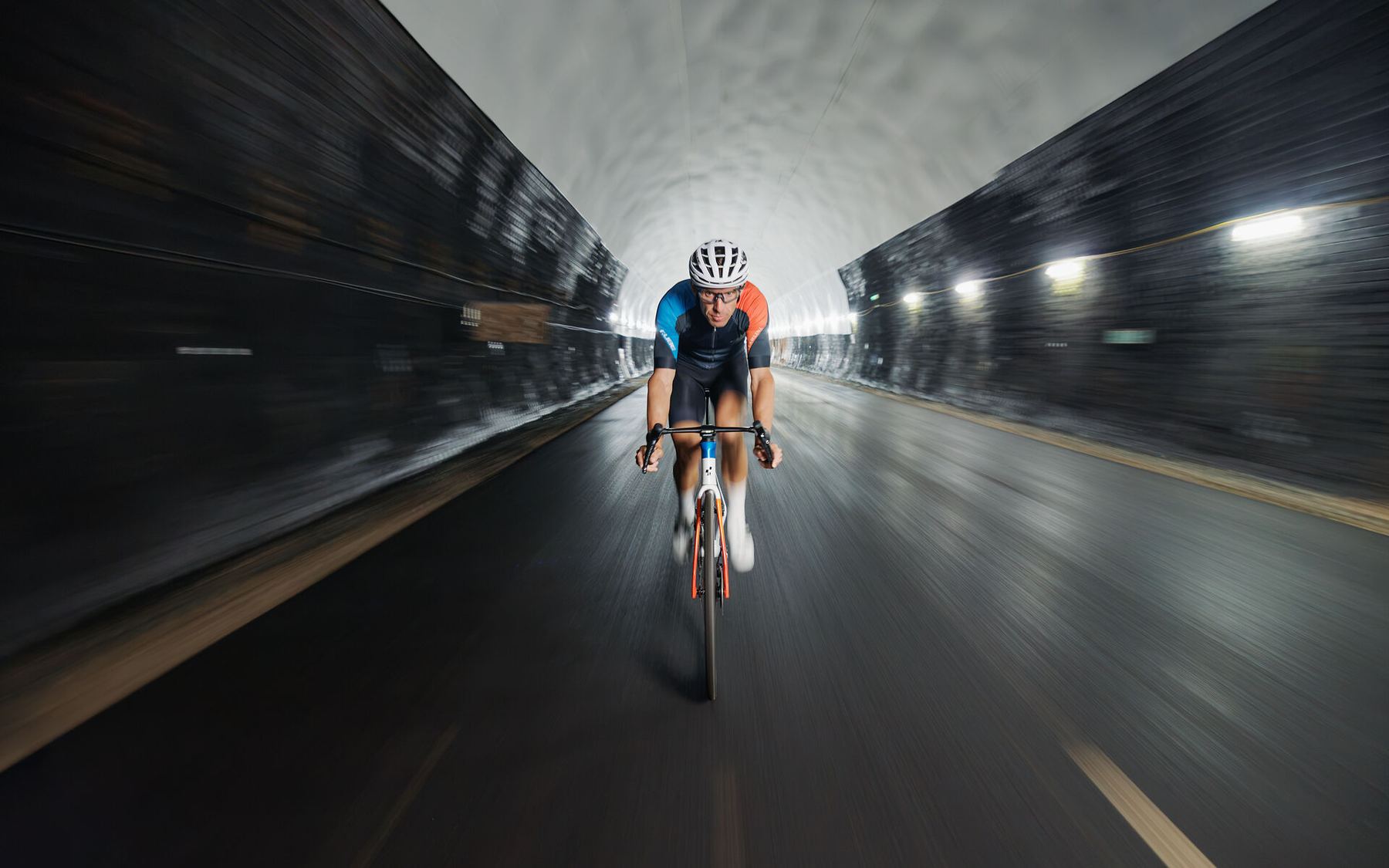 Rennradfahrer in Renntrikot fährt durch einen beleuchteten Straßentunnel