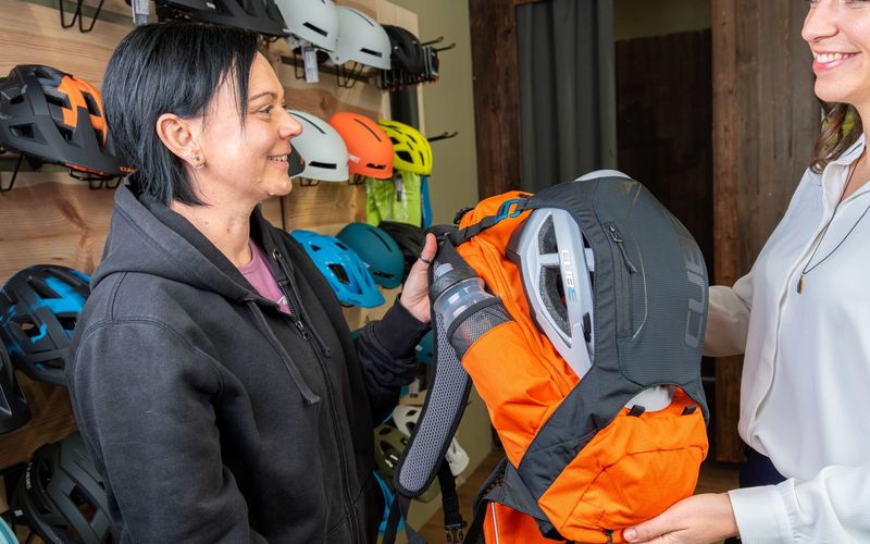 Kundin lässt sich vor der Helmwand einen Fahrradrucksack zeigen