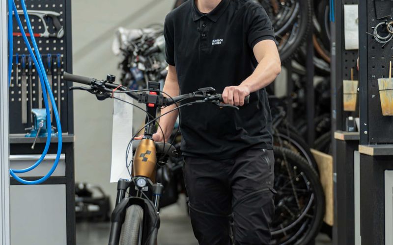 Mechaniker schiebt ein Fahrrad durch die Werkstatt