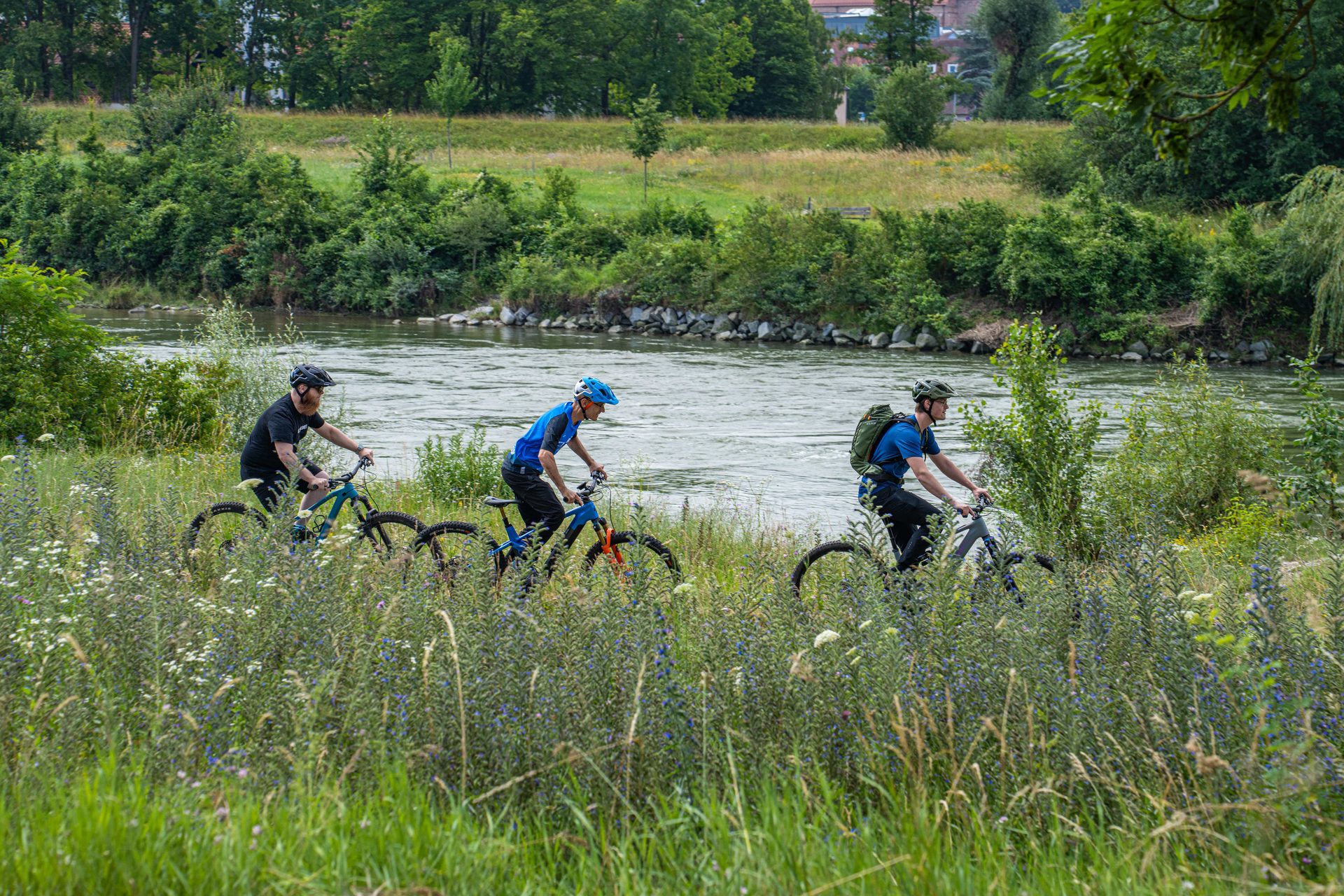 Drei Radfahrer mit Helm auf einem Weg direkt am Ufer der Isar