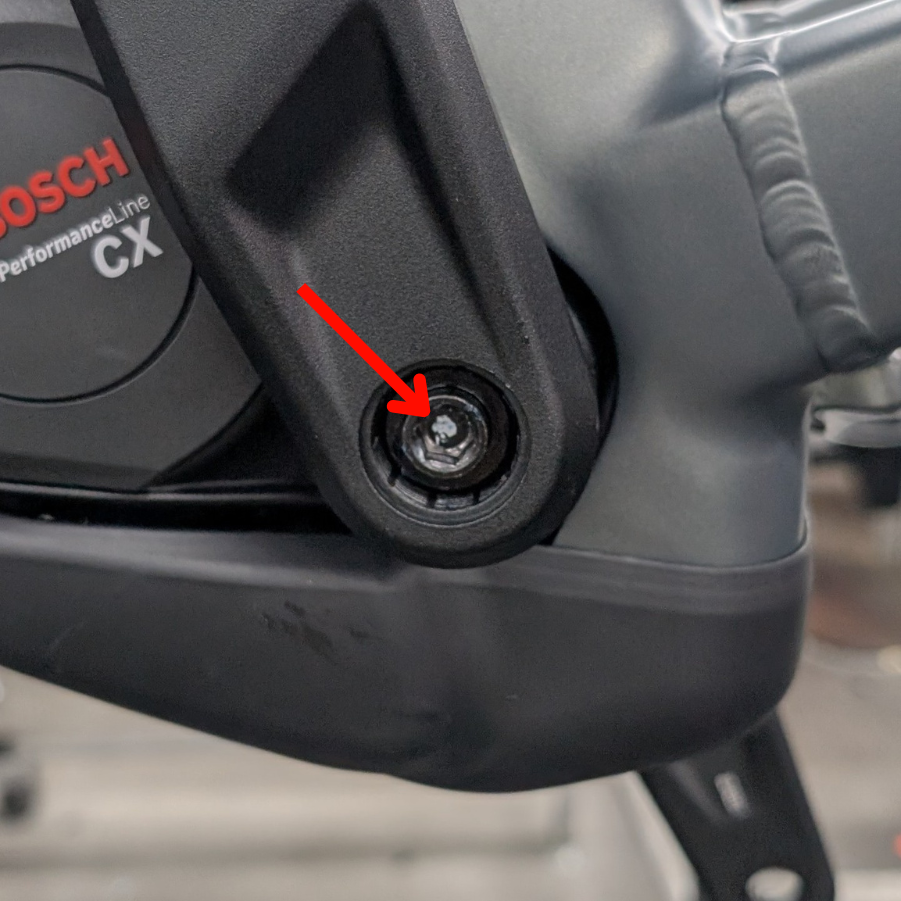 Nahaufnahme eines Bosch Performance Line CX-Elektroradmotors mit einem roten Pfeil, der auf eine glänzende, silberne Schraube in einer schwarzen, runden Aussparung am Motorgehäuse zeigt.